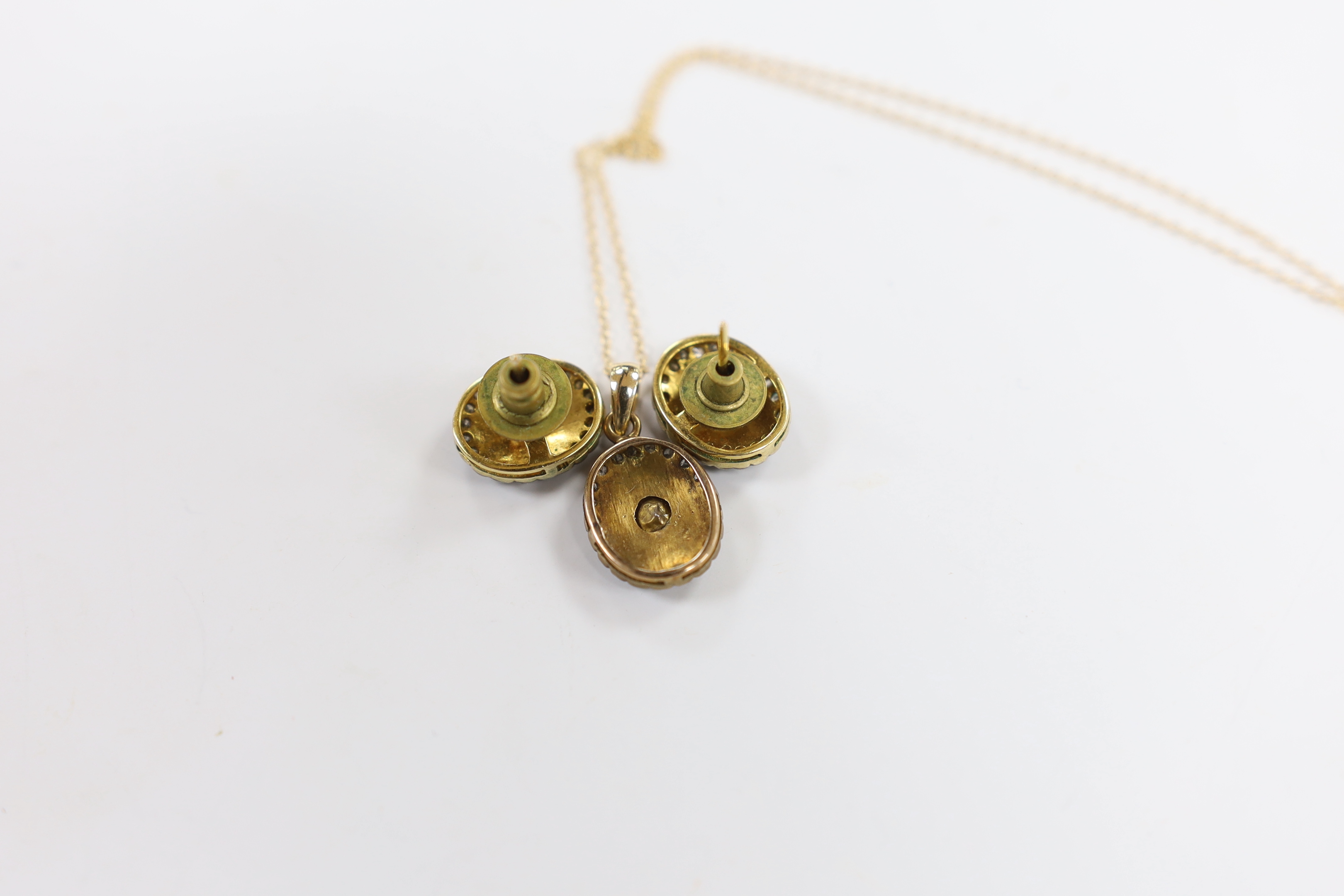A suite of Indian yellow metal and diamond cluster set suite of jewellery, comprising an oval pendant (overall 22mm), on a 14k chain, 44cm and a pair of matching earrings, 14mm, gross weight 8.2 grams.